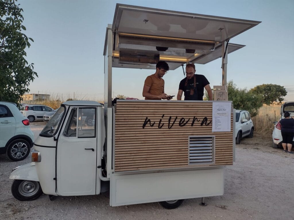 Ape Car Nìvera aperta al tramonto con due bartender al bancone e la drink list del ricevimento appesa, in una campagna siciliana